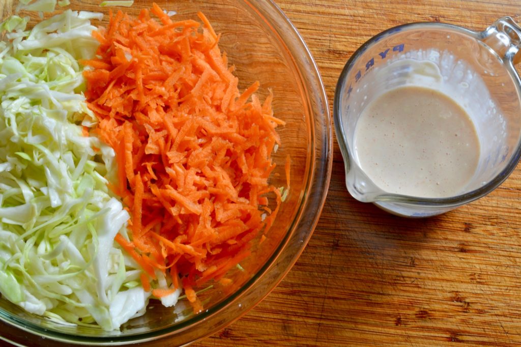 shredded cabbage and carrot in a bowl with coleslaw dressing on the side