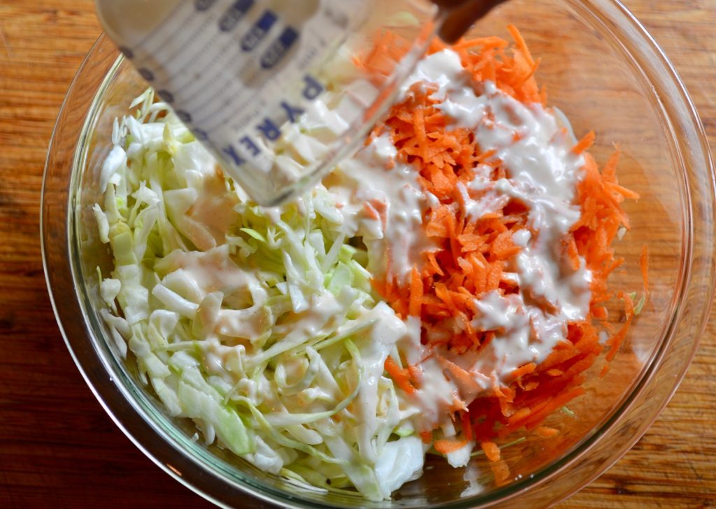 Shredded cabbage and carrot in a bowl with coleslaw dressing being poured on top