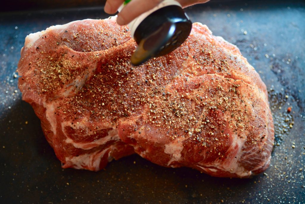 Using a spice container to evenly distribute spice rub on pork butt